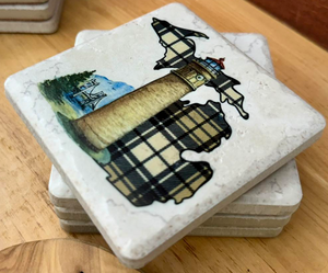 Stack of stone coasters with lighthouse design on a wooden surface
